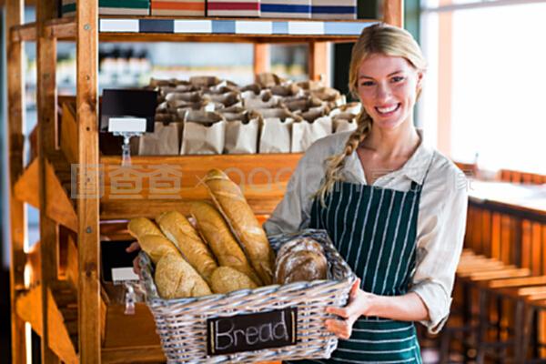 微笑的女性工作人员拿着一篮子面包在柜台旁